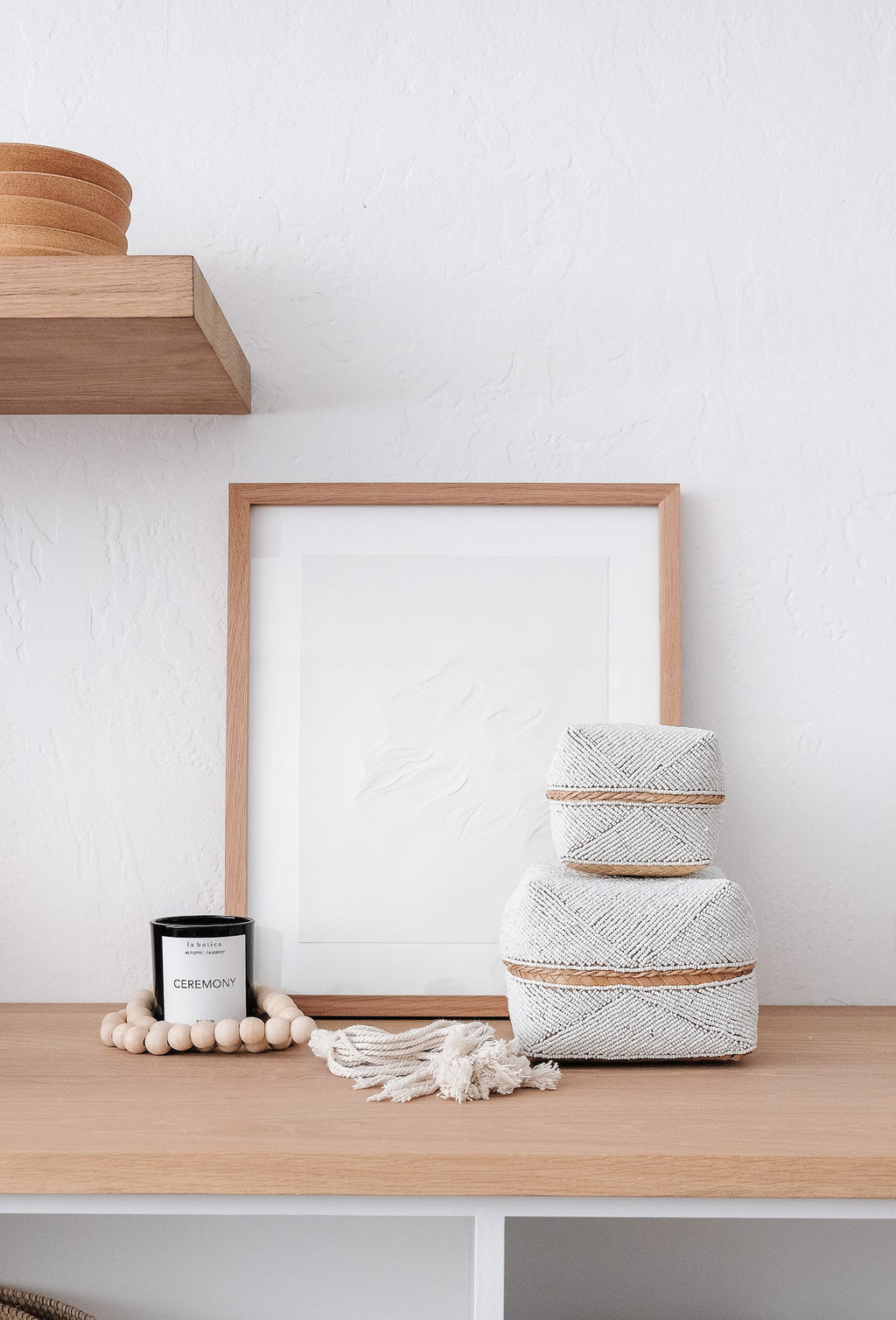 Stacked hand-beaded Bali baskets in solid white on a wooden shelf beside decor items