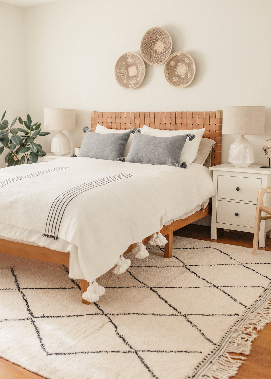 Cozy bedroom with grey Moroccan pom pillow on bed featuring handwoven pom accents and natural decor
