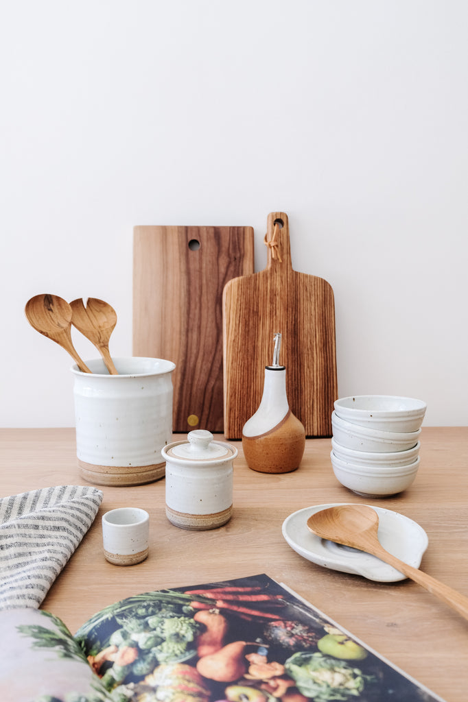 Styled Hanselmann Pottery Collection with Uzumati Ceramic Olive Oil Bottle and Studio Inko Cutting Boards on an Oak Dining table against a white wall. - Saffron and Poe
