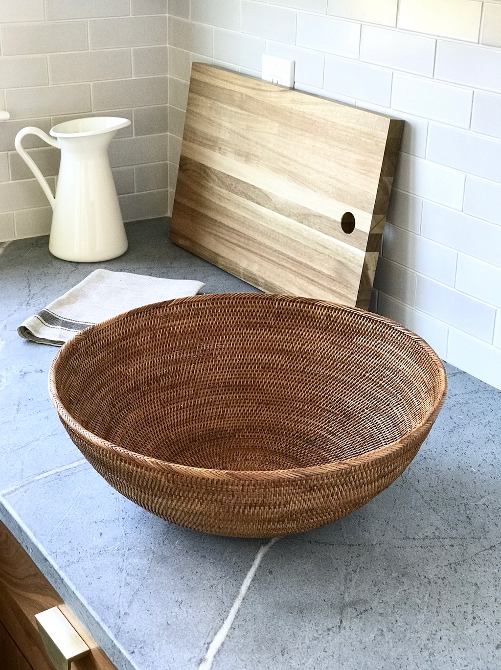 Woven Tenganan basket made from natural Ata reed displayed on kitchen counter with cutting board and white pitcher in background