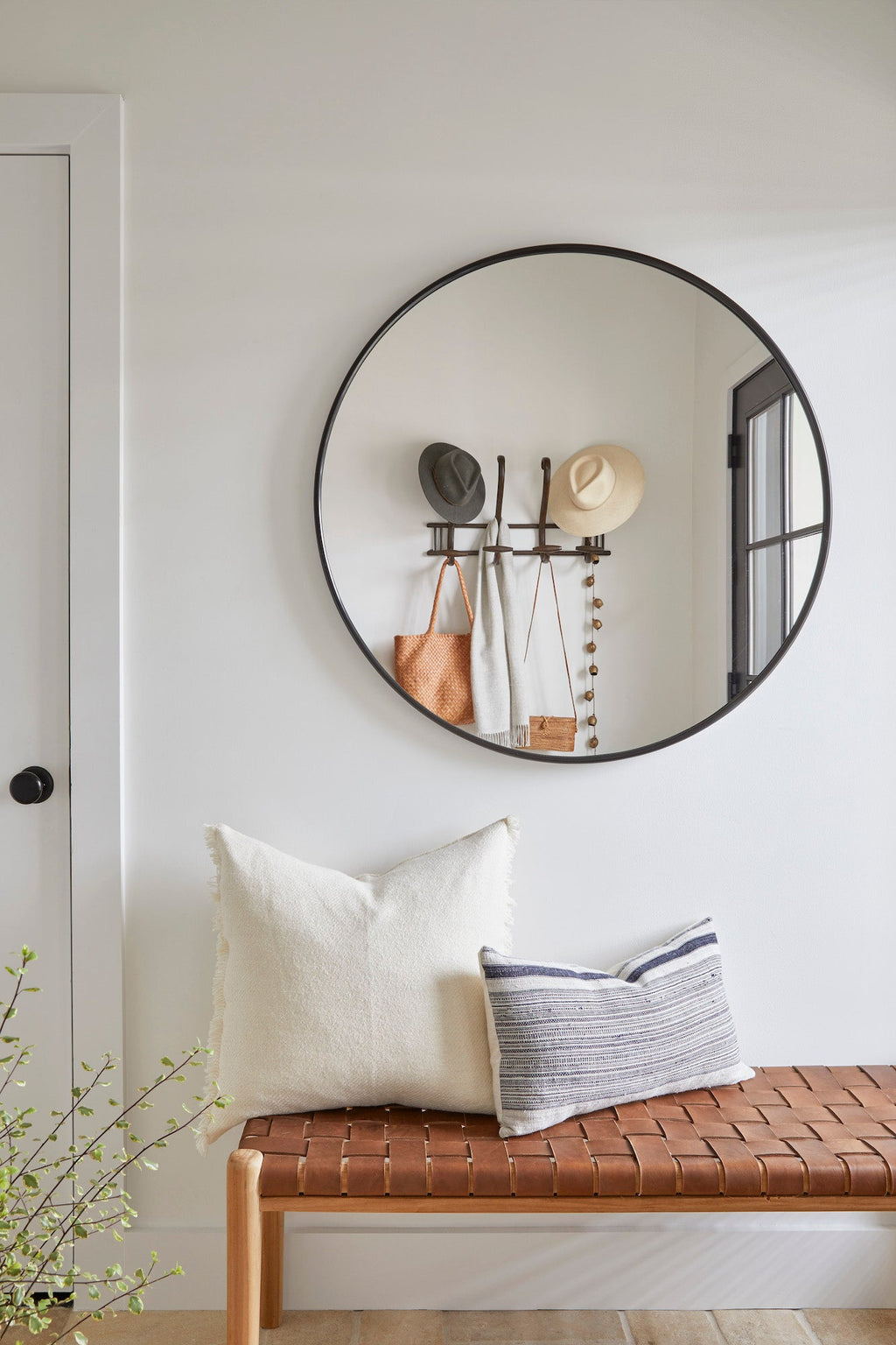 Ivory baby alpaca pillow on woven bench in modern minimalist room with round mirror and hats hanging on wall