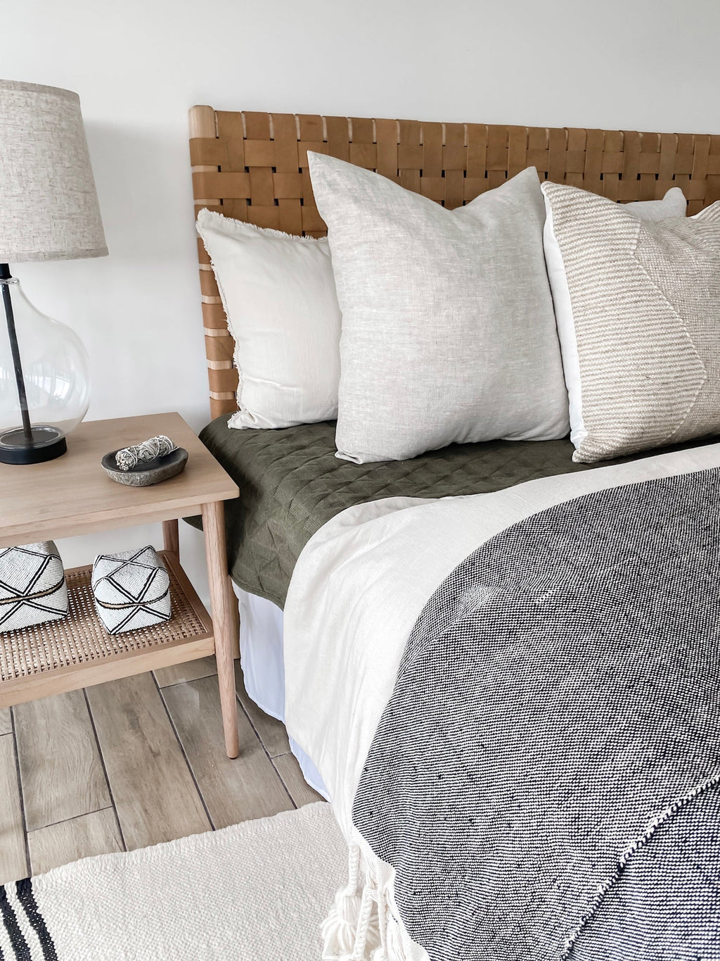Natural linen pillows on bed with woven headboard and bedside table lamp