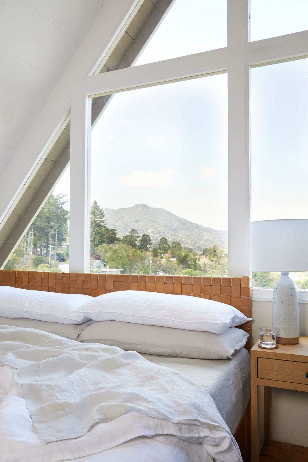 Natural linen sheet set on a bed in a bright room with large windows and mountain view