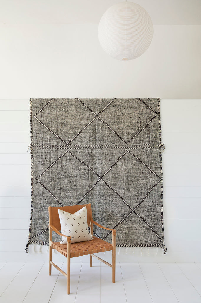 Styled view of No. 27 - Moroccan Flat Weave Kilim Rug with a Leather Strap Safari Lounge Chair against a white background. - Saffron and Poe