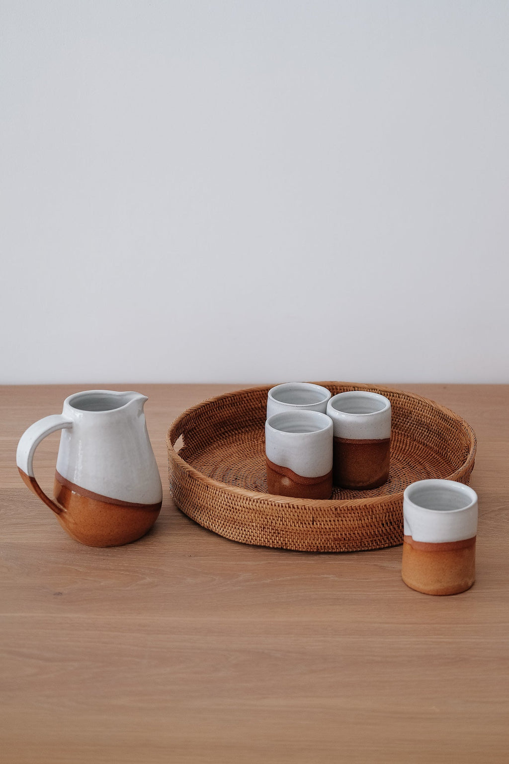 Round Tenganan Basket Trays with ceramic pitcher and cups on wooden surface
