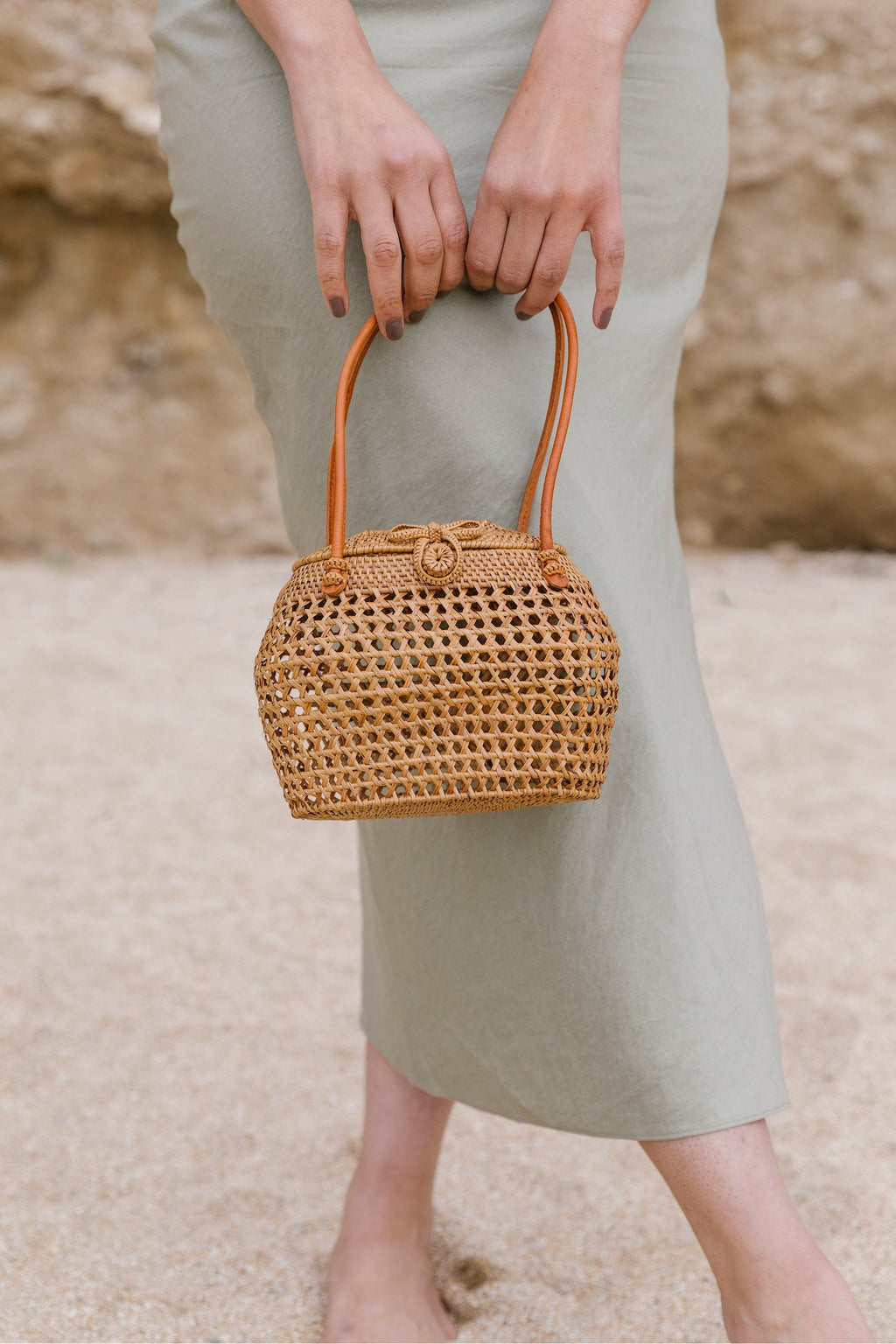 Tenganan Basket Clasp Handbag with rattan-style weave and leather loop straps held by person in light green dress