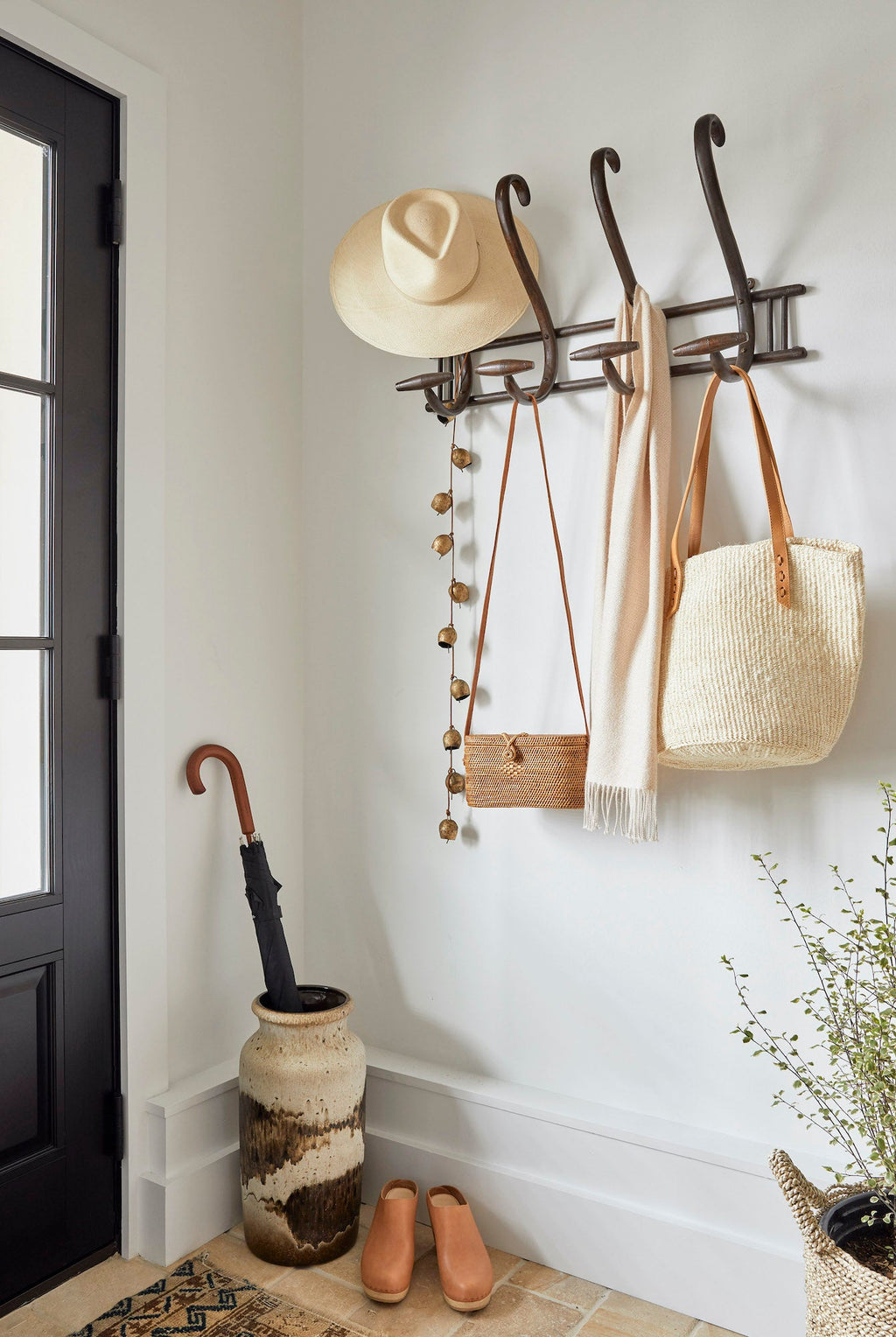 Tenganan Basket Crossbody bag hanging on wall hook with hat, scarf, and tote in entryway