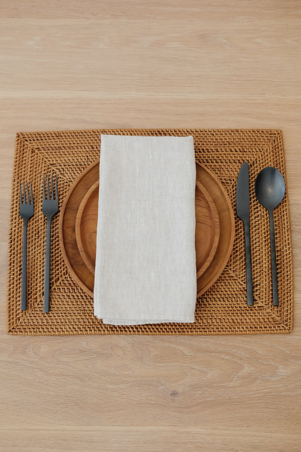 Intricately woven rectangular Woven Tenganan Placemat made from natural Ata reed with wooden plate, white napkin, and black cutlery on wooden table