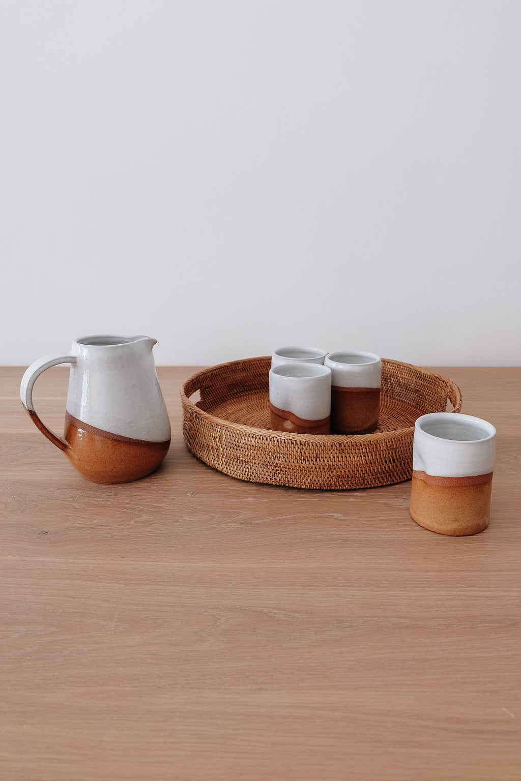 Uzumati Drifter Pitcher with white and rust stoneware alongside matching cups on wooden surface