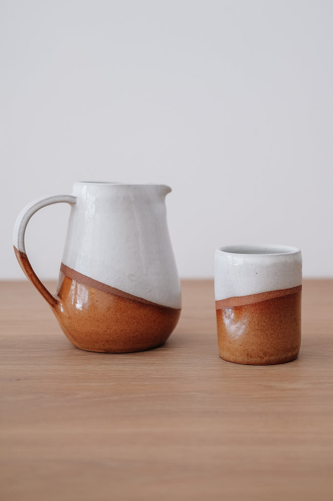Styled Uzumati Drifter Pitcher with a Drifter Tumbler on a White Oak Table against a white wall. - Saffron and Poe