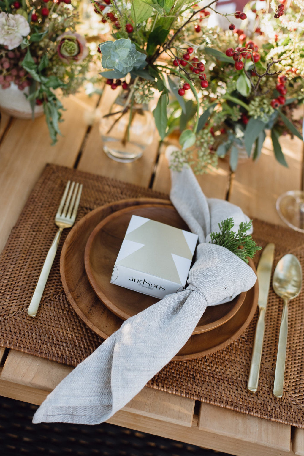 Natural linen napkin tied around wooden plate on elegant dining table with gold cutlery and floral centerpiece