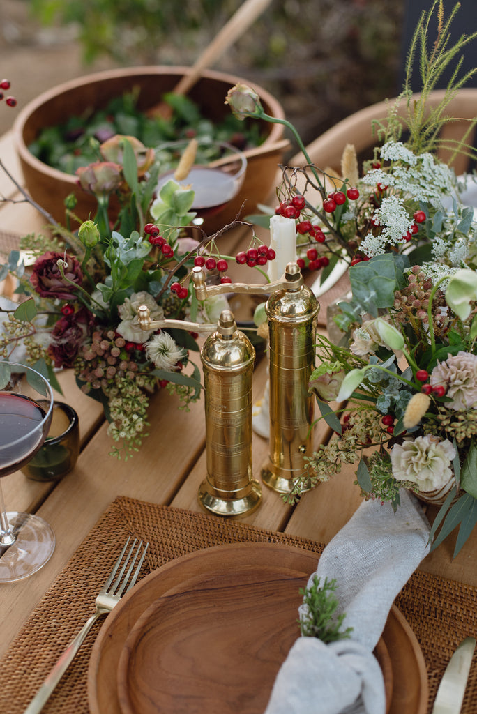 Atlas Brass Salt and Pepper Grinders on an outdoor table with Teak Plates, Teak Salad Bowl, Tenganan Placemat and Holiday florals. - Saffron and Poe