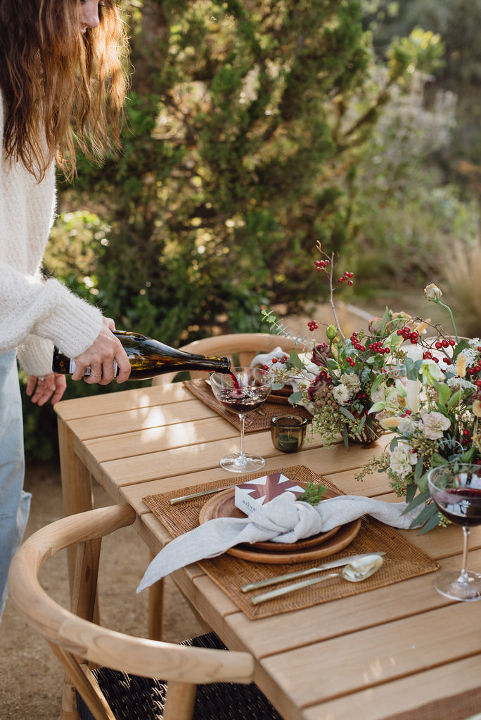 Woven Tenganan Placemat with Teak Plates and Natural Woven Napkin on an outdoor table setting with holiday florals. - Saffron and Poe