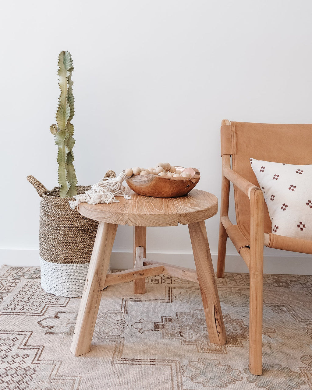 Vintage round side table handcrafted from reclaimed elmwood beside a tan armchair and cactus plant in woven basket on patterned rug