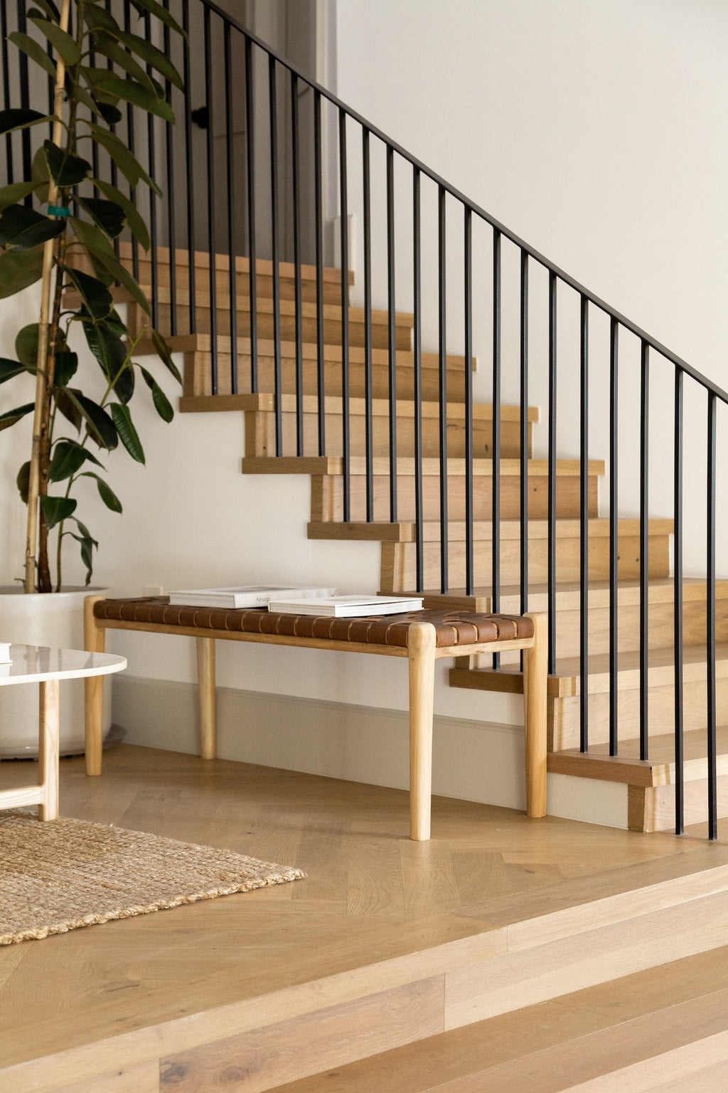 Woven leather bench with teak frame under wooden staircase in modern home interior