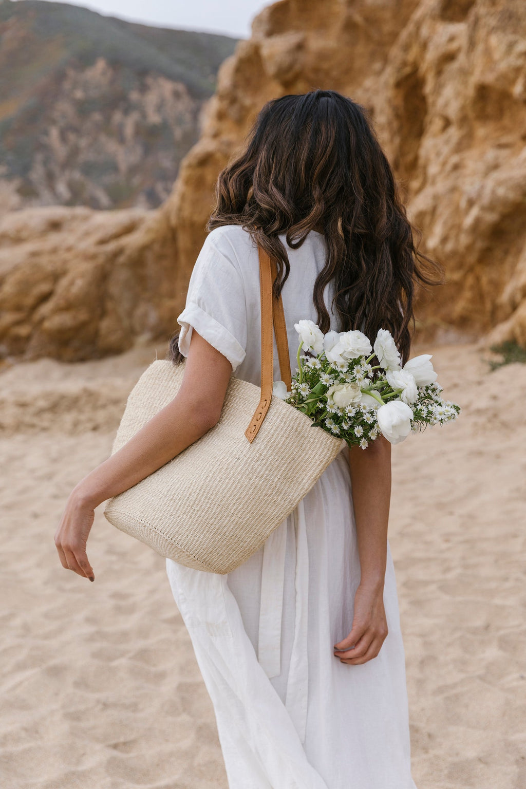 Woven Sisal and Leather Tote with leather straps carried by woman at beach with flowers inside