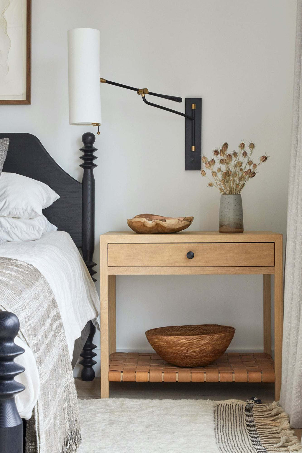 Woven Tenganan basket on wooden bedside table with bed and wall lamp in bedroom setting