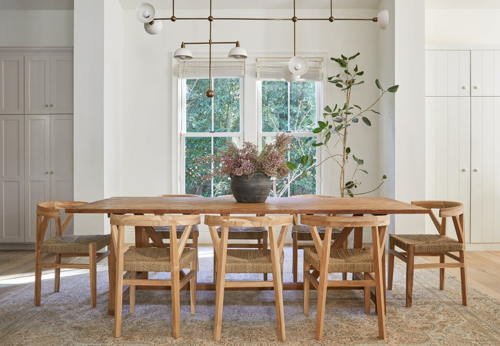Dining room with wooden woven wishbone dining chairs and a wooden table under modern chandelier near large windows