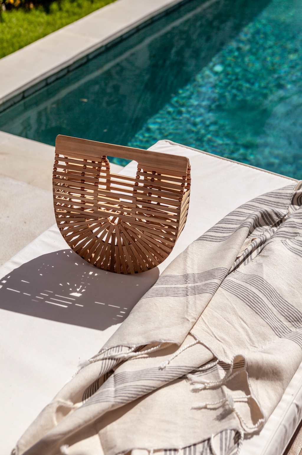 Bamboo Crescent Clutch handcrafted from natural bamboo resting by poolside on striped fabric.