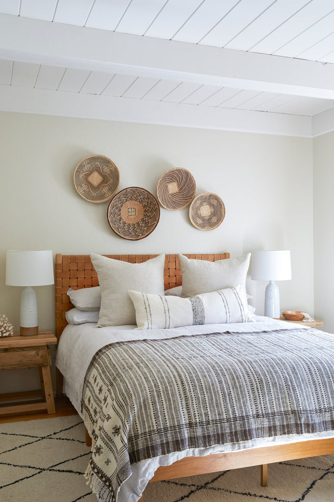 Styled front view of Ilala basket set above beige woven leather headboard with hand thrown ceramic lamps and vintage elmwood side tables. - Saffron and Poe