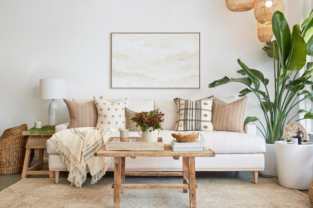 Styled shop view of our Handwoven Colombian Throw in grey draped over sofa with decorative pillows, Ceramic Lamp, Vintage Coffee Table, Vintage Side Table, Aleksandra Zee art work, Turkish Rug, and Terrazzo side table. - Saffron and Poe