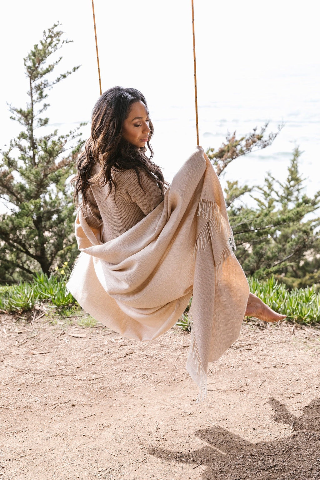 Woman wrapped in beige baby alpaca throw blanket sitting on outdoor swing