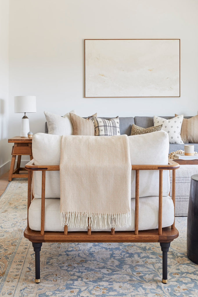 Styled Alpaca Throw - Beige against a wooden framed chair in a bright living room. - Saffron and Poe