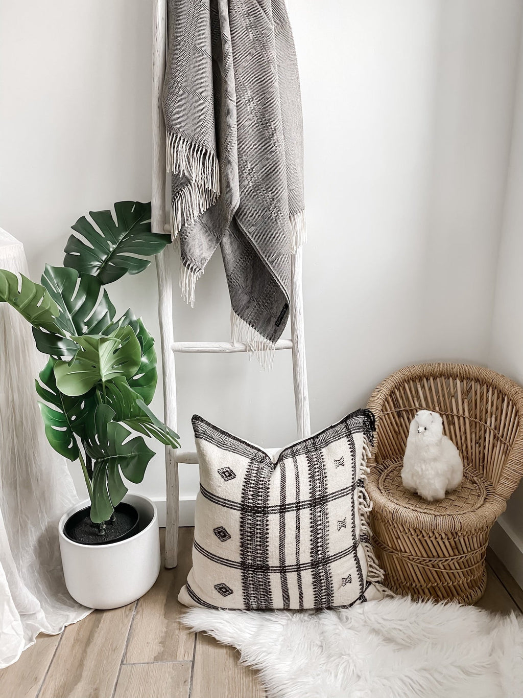 Charcoal brown baby alpaca throw with geometric pattern hanging on a white ladder next to a woven chair and patterned pillow in a cozy room corner