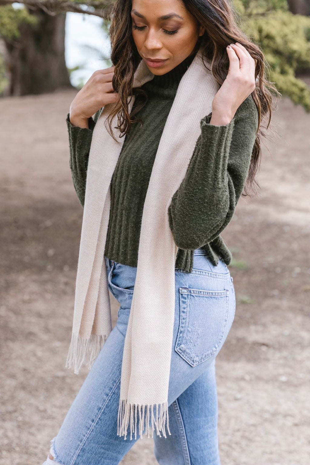 Woman wearing beige baby alpaca scarf with fringe and green sweater outdoors