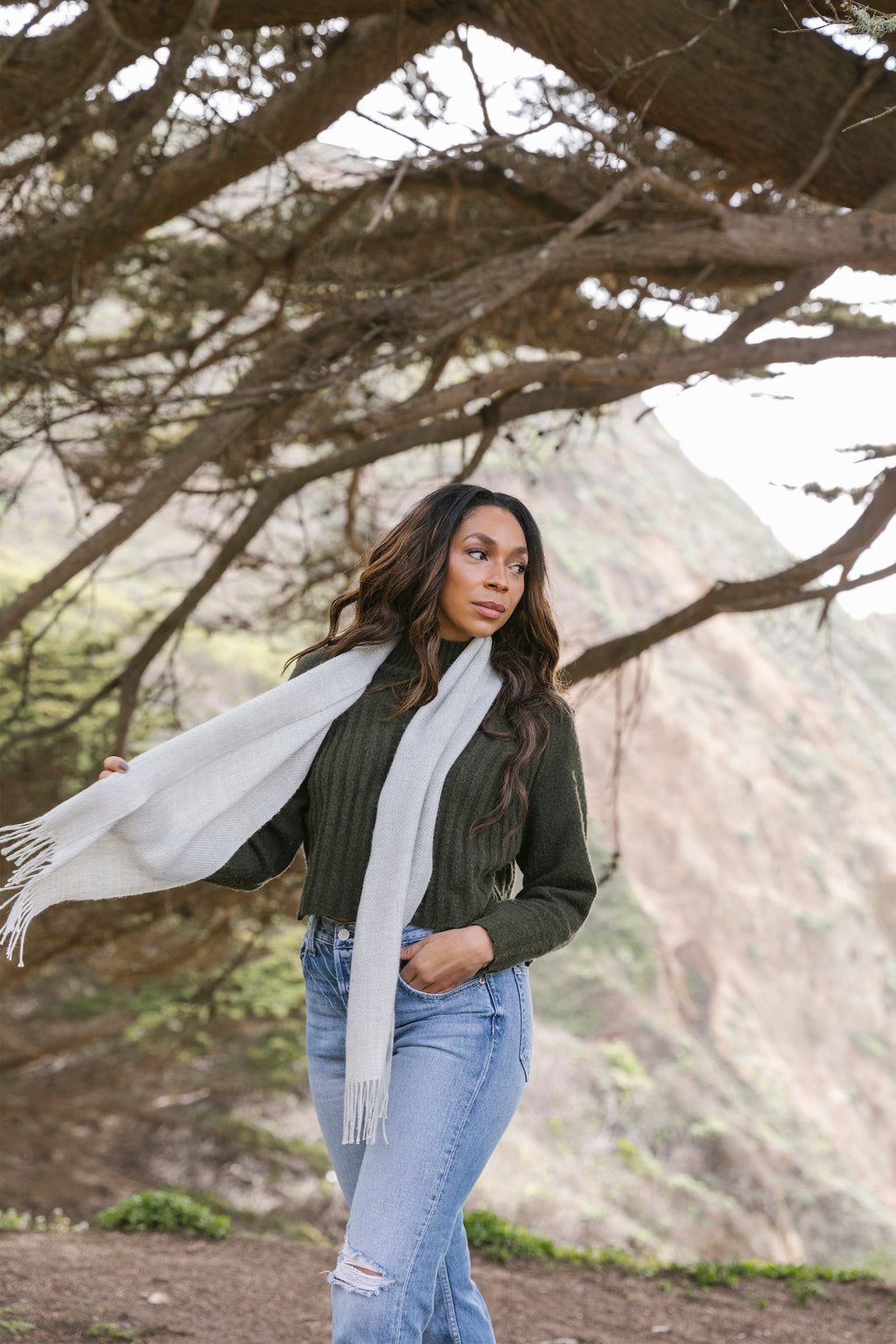 Woman wearing gray baby alpaca scarf outdoors near trees and mountains
