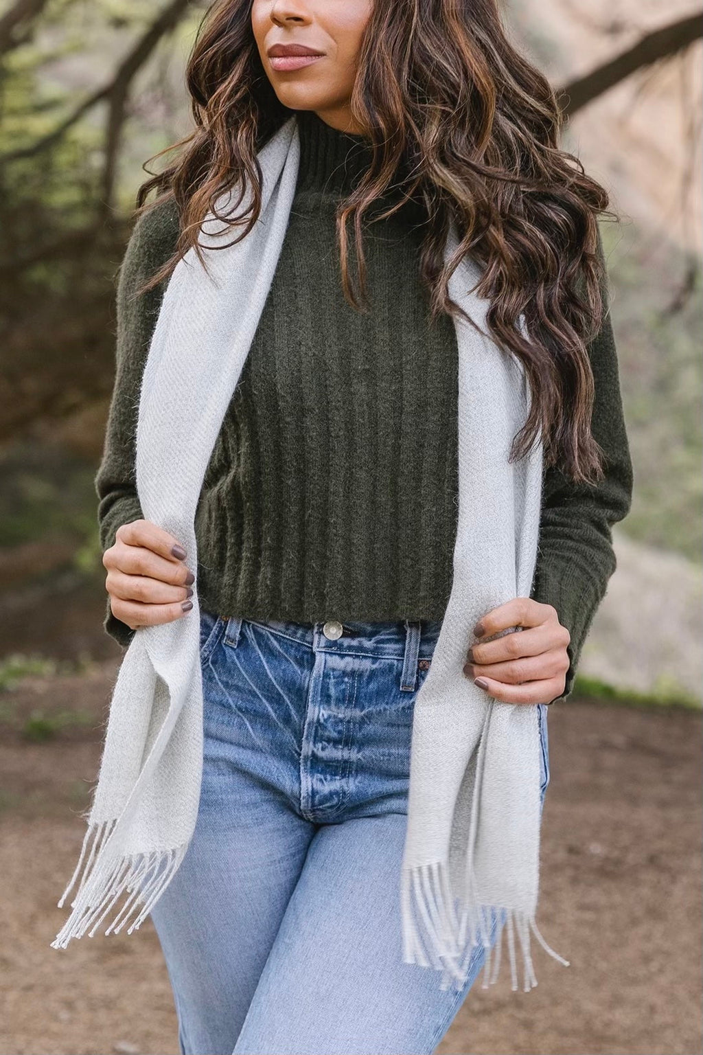 Woman wearing gray baby alpaca scarf with fringes over dark green sweater and jeans outdoors