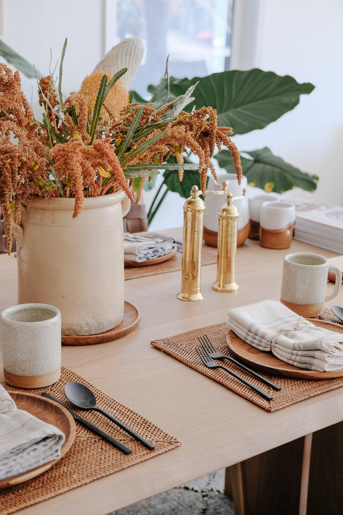 Styled Italian Confit Pot with seasonal florals on a dining table with Tenganan Placemats, Teak Plates, Linen Napkins, Uzumati Ceramic Mugs, and Brass Grinders. - Saffron and Poe