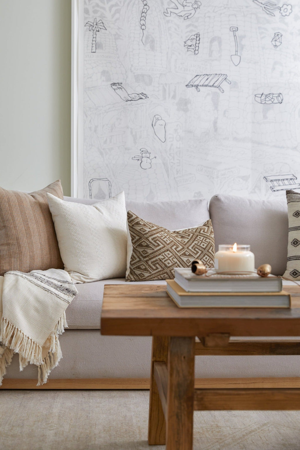 Beige embroidered pillow on sofa with neutral textured accents and wooden coffee table with candle and books