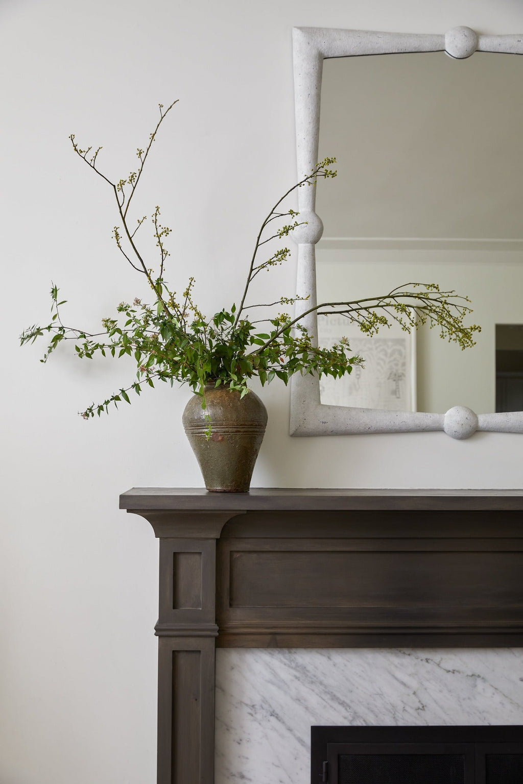 Vintage Mijiu jar with dried branches on a mantelpiece under a white-framed mirror