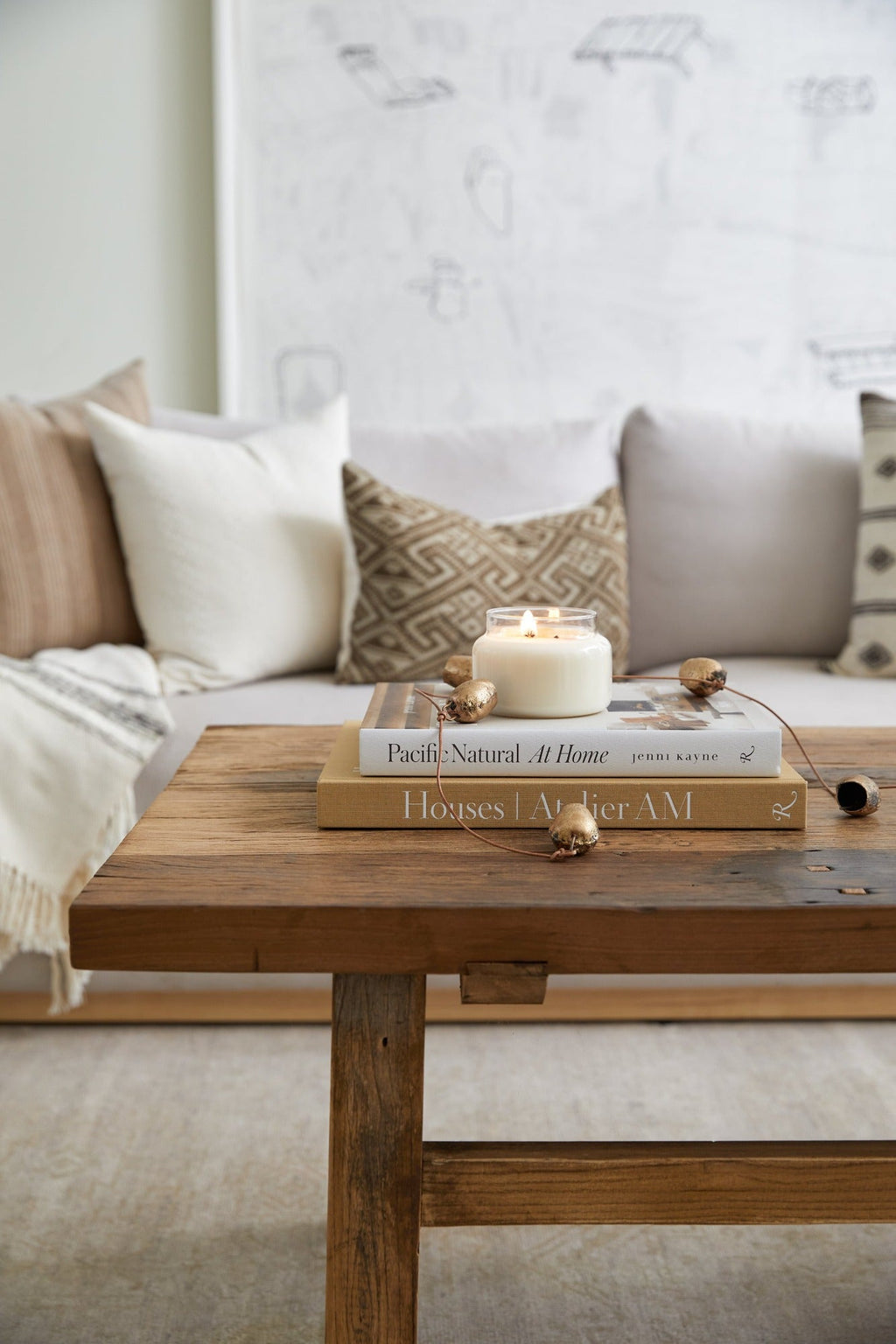 Cozy living room with textured pillows, wooden coffee table, stacked design books, and a lit candle showcasing Pacific Natural: At Home aesthetic