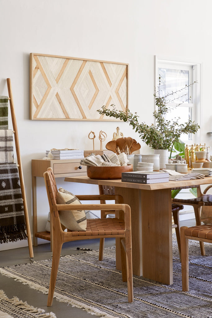 Styled side view of the Woven Leather Strap Dining Arm Chair in Beige in a dining room setting with Aleksandra Zee art work, Oak Console Table, Oak Dining Table, and Moroccan Rug. -  Saffron and Poe.