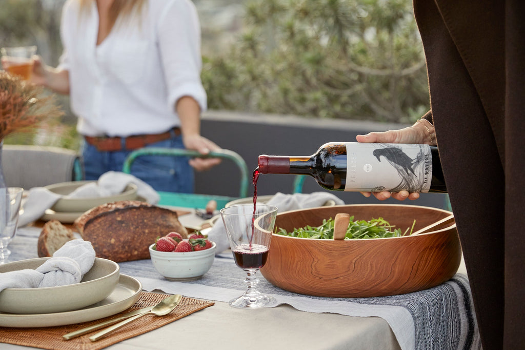 Outdoor dining table set with vintage striped table runner, wooden salad bowl, and wine being poured into a glass
