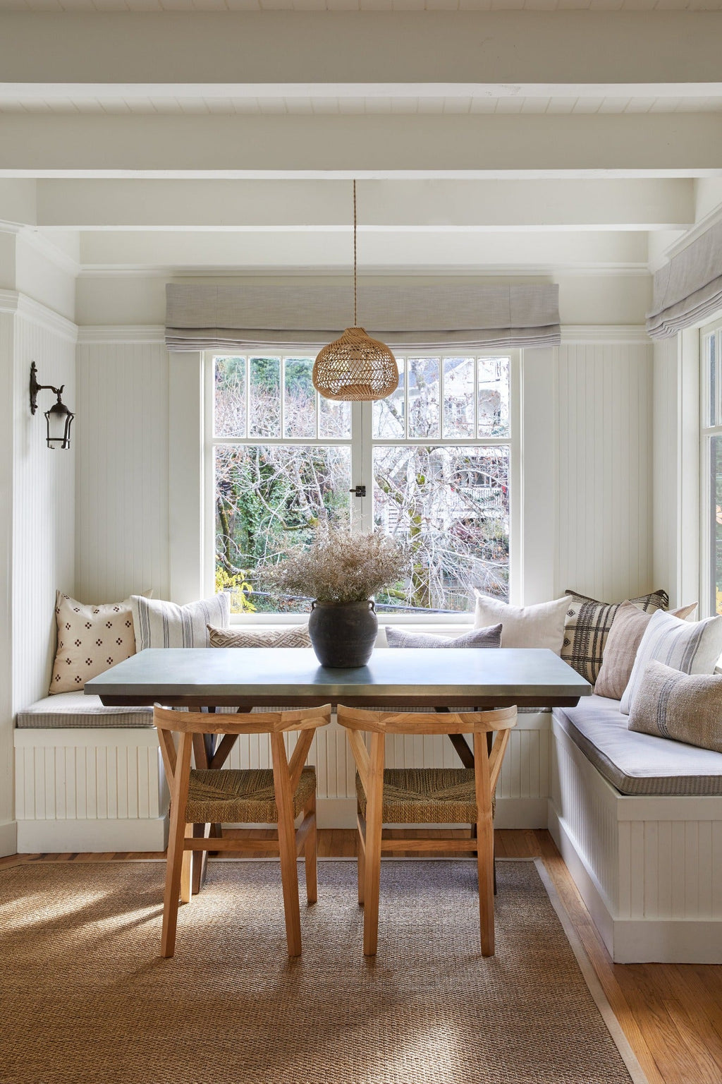 Round Basket Pendant hanging above dining table in cozy breakfast nook with natural wood chairs and built-in bench seating