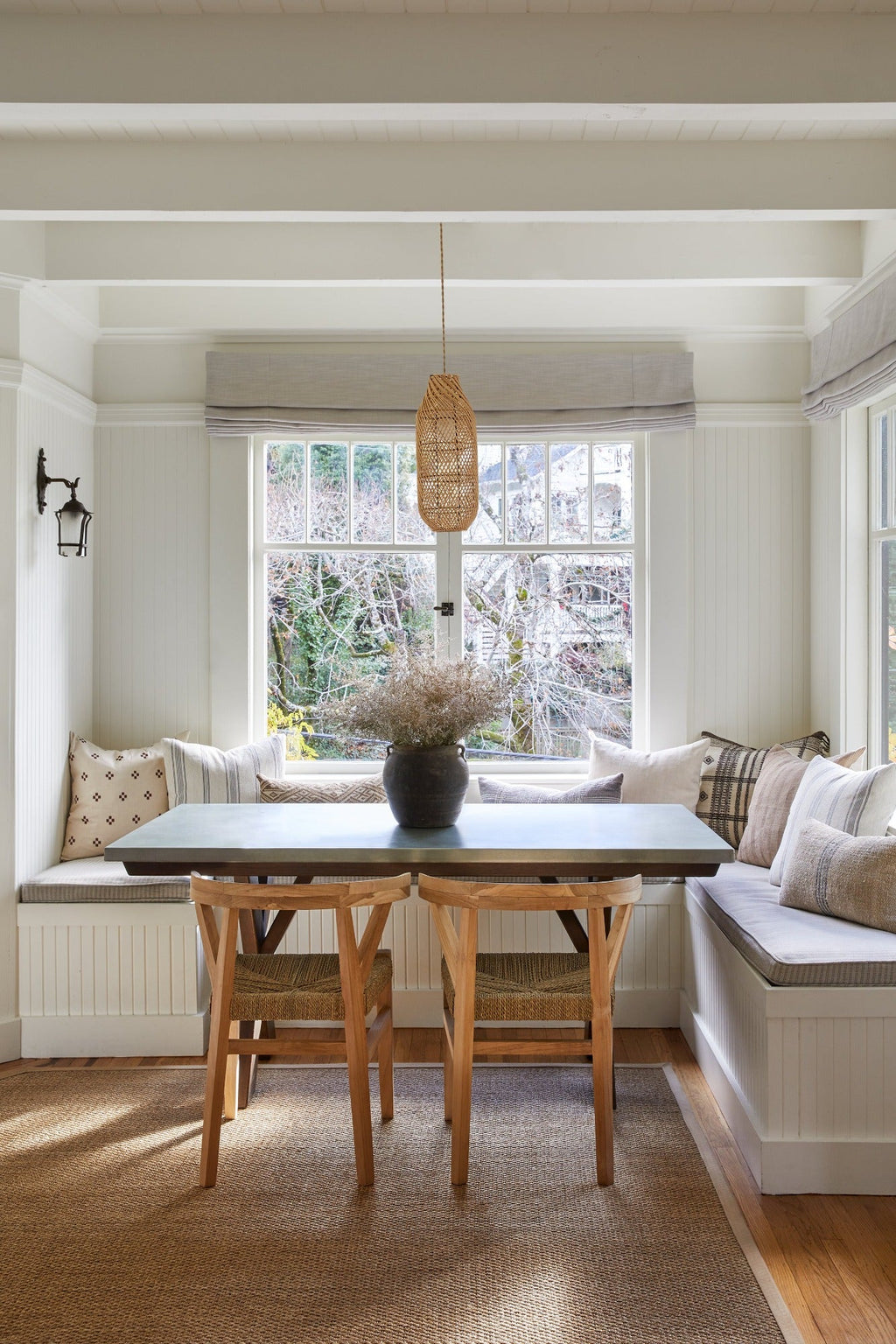 Oblong basket pendant light hanging above wooden dining table in cozy breakfast nook with bench seating and natural decor