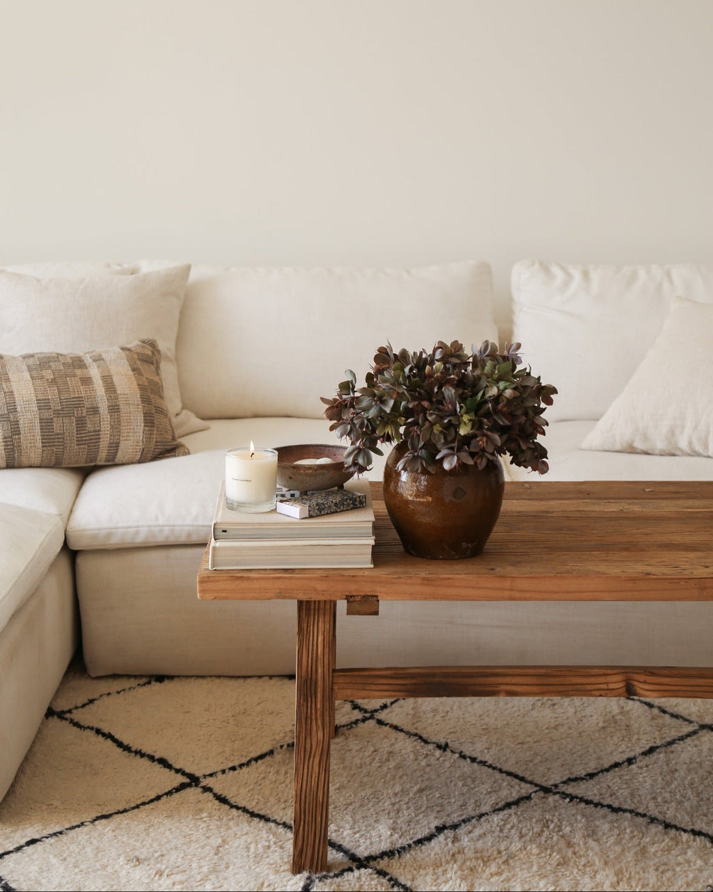 Vintage wood coffee table in dark elm with decorative books, candle, and plant on top in modern living room setting