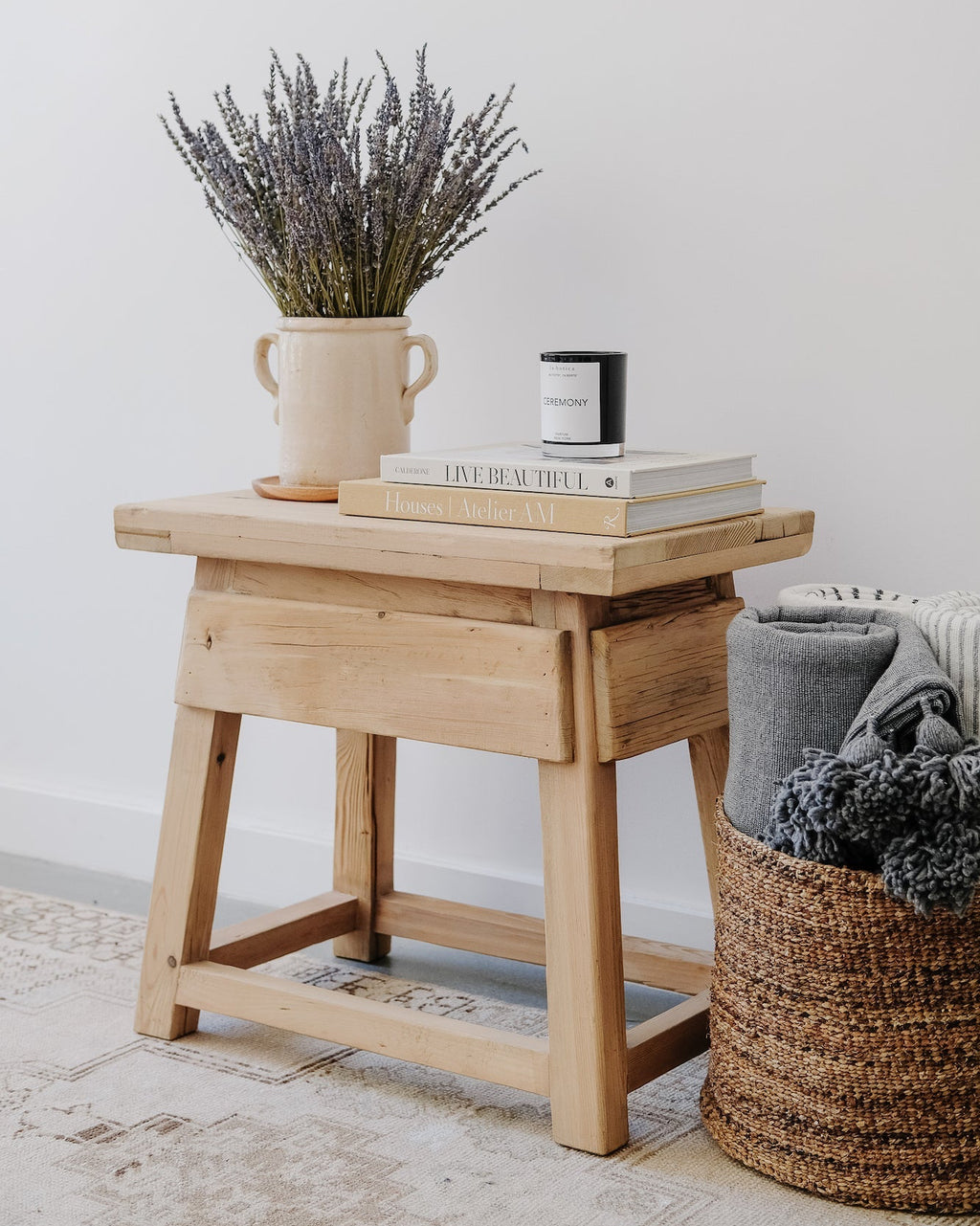 Vintage cedar end table with rustic finish styled with books and vase in a minimalist living space