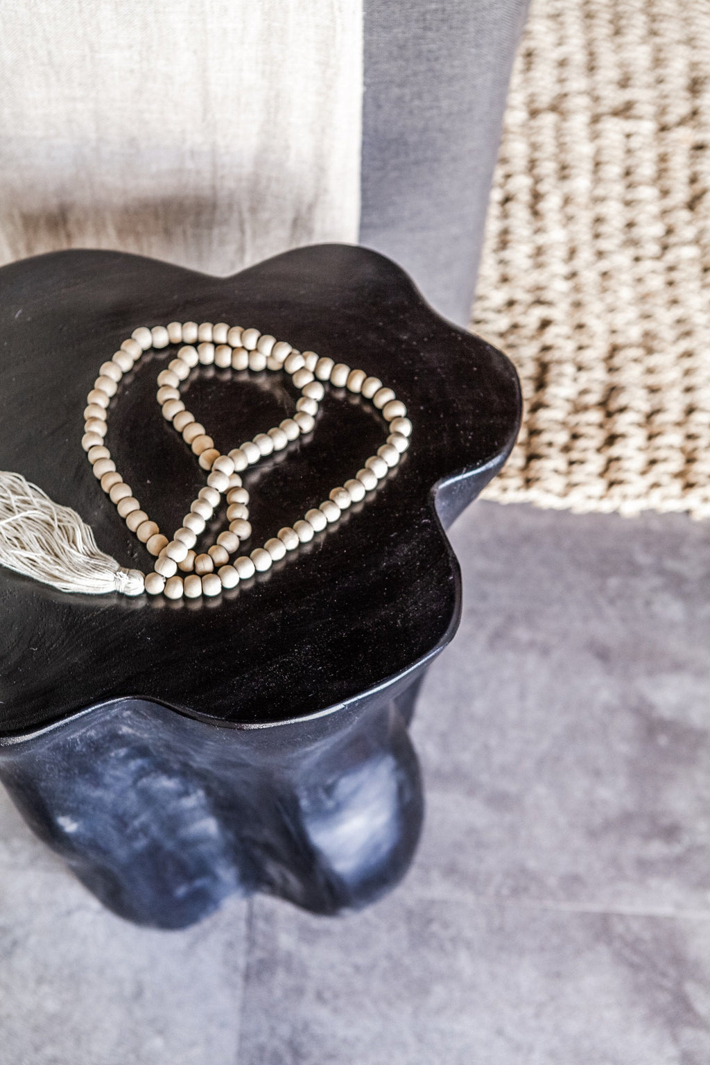 Tasseled wooden Bali beads with cream tassel draped on dark wooden stool surface