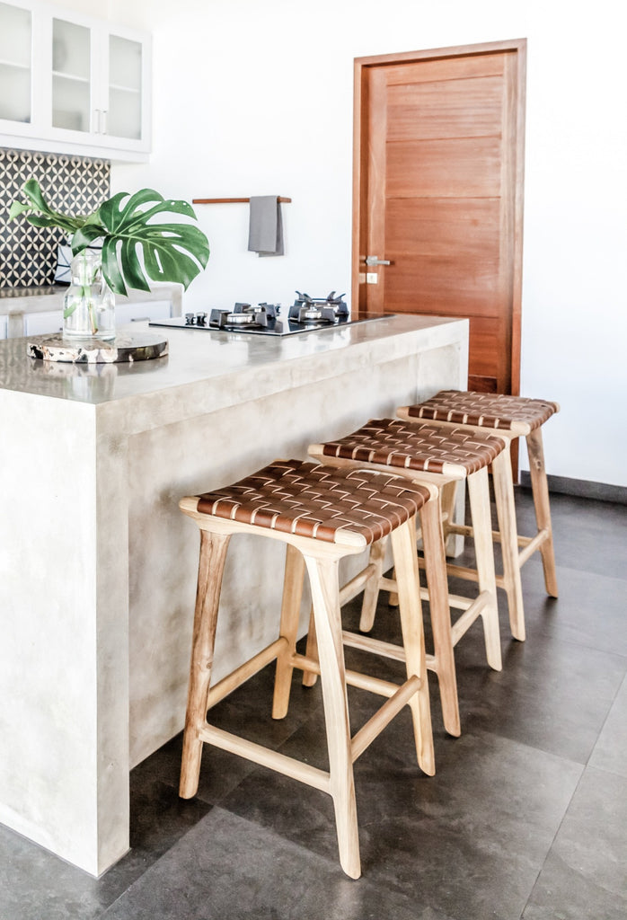 Three counter height Backless Woven Leather Counter dining stool in the kitchen. Handmade in Bali using Teak wood and vegetable-tanned leather imported from Java. - Saffron and Poe