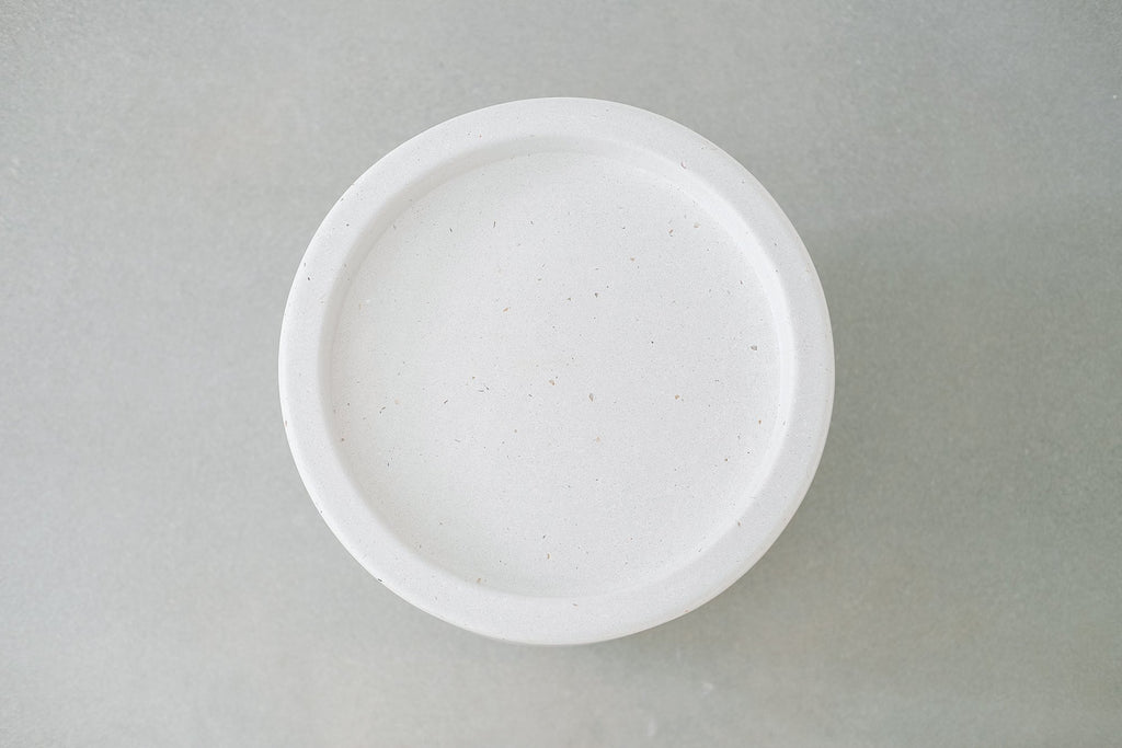 Top view of a handmade white abalone terrazzo side table with flecks of shell on a gray surface