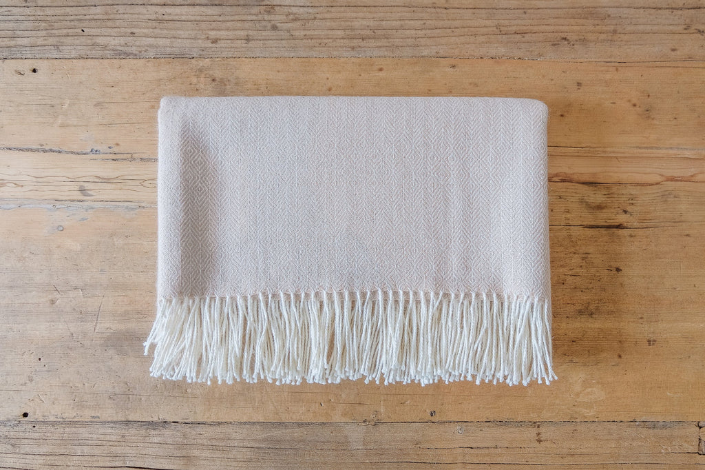 Beige baby alpaca throw blanket with geometric pattern and fringed edges on wooden surface