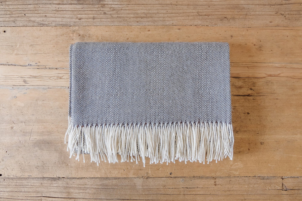 Charcoal brown baby alpaca throw blanket with geometric pattern and white fringe on wooden surface