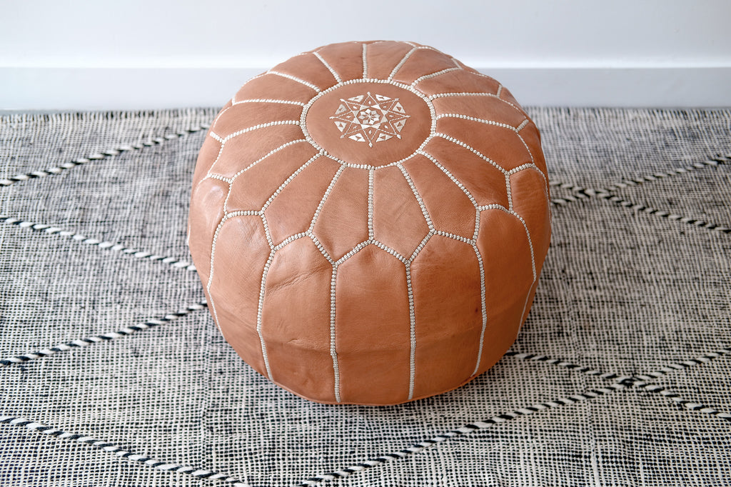 Top angled view of Embroidered Leather Moroccan Pouf on a Moroccan Kilim Rug against a white wall. - Saffron and Poe