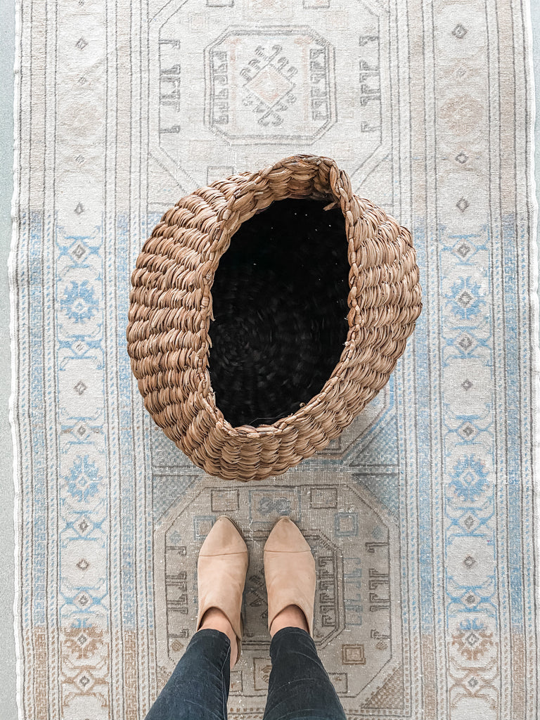 Top view of sculptural nest basket on Turkish oushak rug with model standing in front - Saffron and Poe