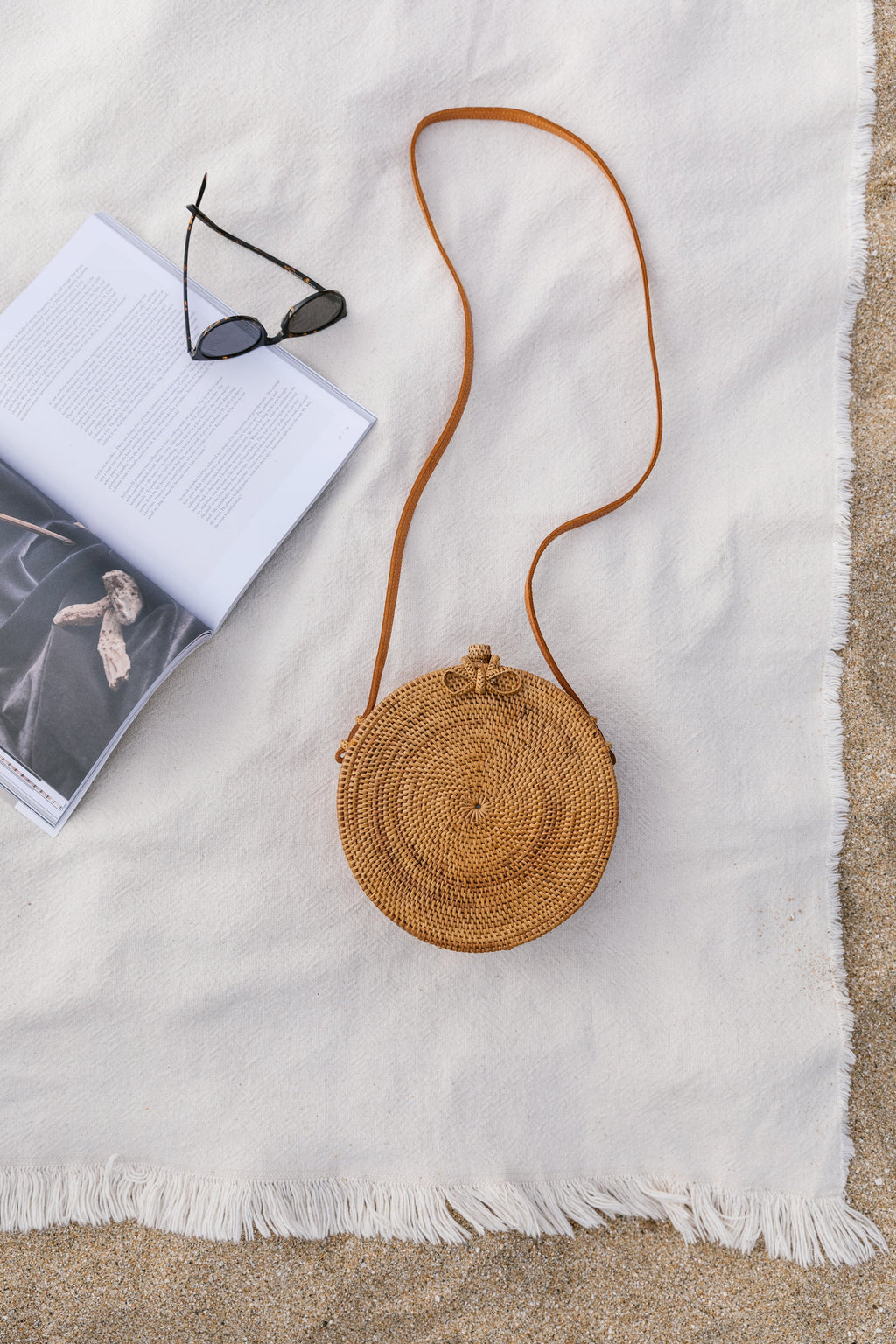 Round Tenganan Basket Crossbody bag made of woven Ata reed with leather strap on white fabric background