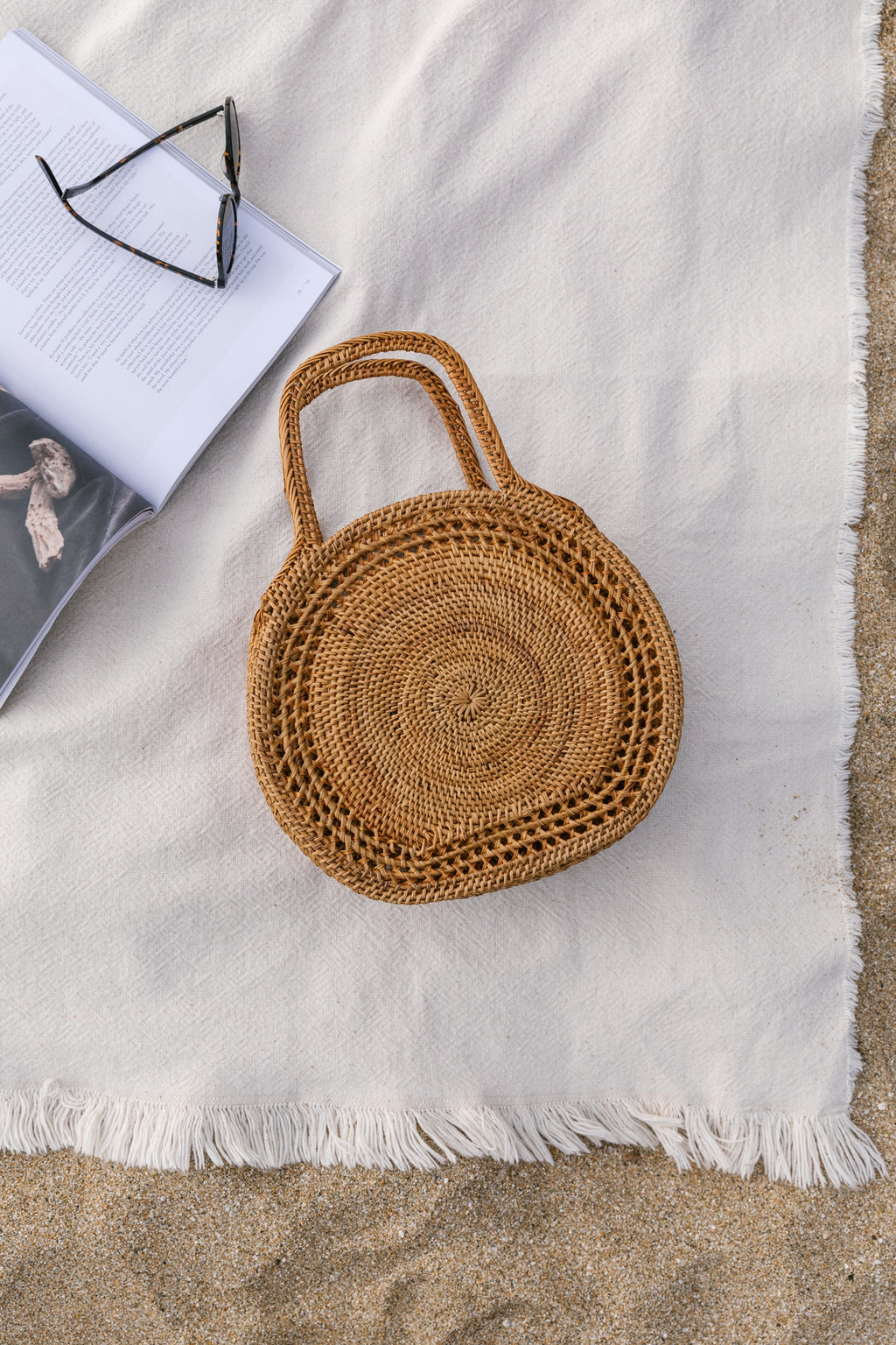 Tenganan Basket Handbag made of handwoven natural Ata reed with concentric circle weave placed on white fabric near a magazine and glasses